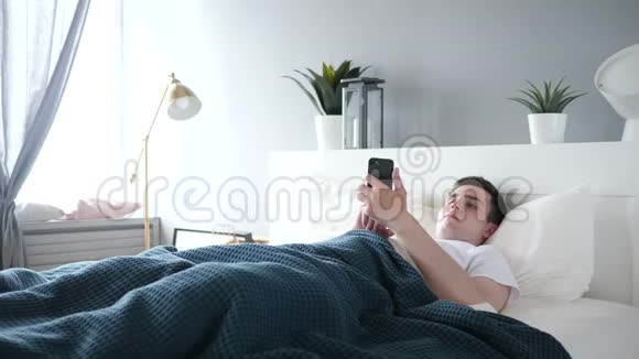 男人躺在床上用智能手机视频的预览图