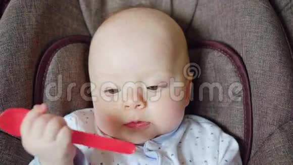 可爱的婴儿躺在婴儿车里吃着红勺子视频的预览图