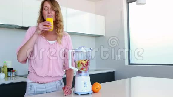 厨房里的美女在榨汁机旁边喝橙汁视频的预览图