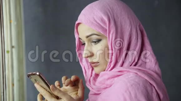 一位美丽的阿拉伯年轻女子站在窗边用手机说话视频的预览图