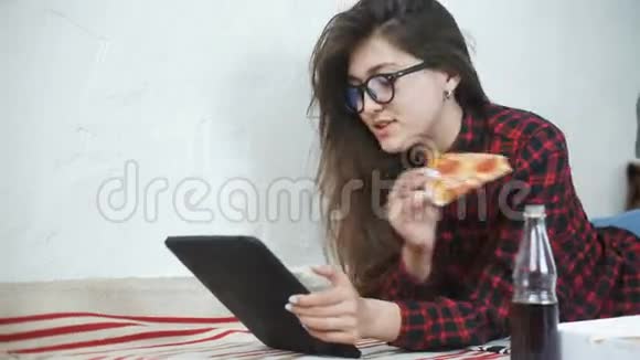 亚洲女人吃披萨在家看数码平板电脑视频的预览图