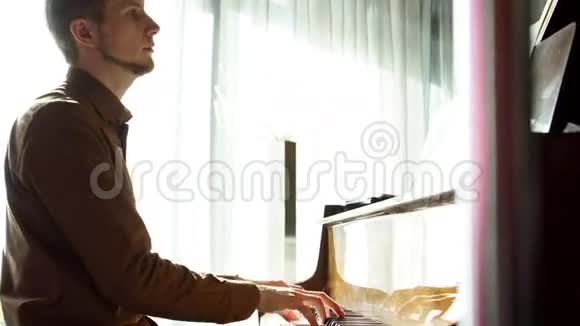 弹钢琴那个年轻人弹钢琴这位美丽的钢琴家演奏旋律室内窗户发出悦耳的灯光视频的预览图