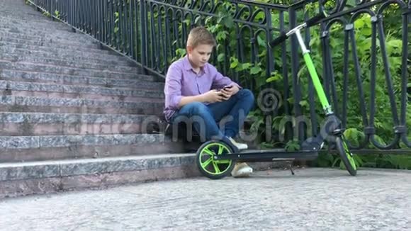 男孩坐在公园的楼梯上写着电话视频的预览图