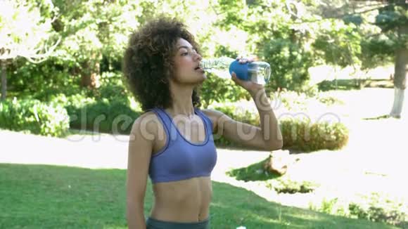 在公园慢跑后一位身材苗条的黑发女人正在喝水视频的预览图