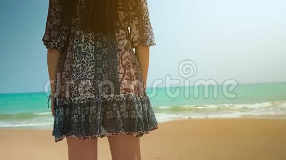 海滩上穿着蓝色裙子的女孩看着海洋近距离射击视频的预览图