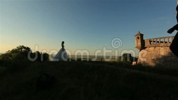 美丽浪漫的新婚夫妇新郎和新娘拥抱在日落的老城堡附近视频的预览图