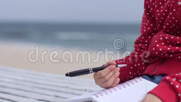 小女孩用手在海边的笔记本上写字视频的预览图