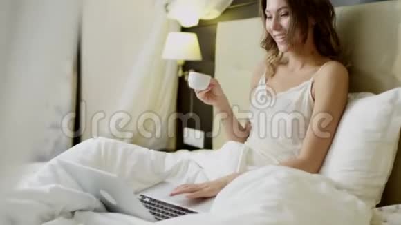 有笔记本电脑的年轻女子在床上喝咖啡视频的预览图