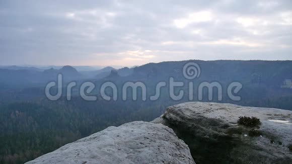 穿着蓝色夹克衫的摄影师站在岩石的视点上拍摄朦胧的早晨景观在岩石里远足视频的预览图