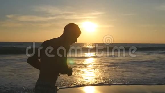 日落时分一个运动的年轻人在海边奔跑日出时运动员沿着海岸慢跑男性视频的预览图