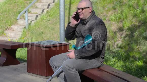 拄拐的残疾人坐在长凳上用智能手机说话视频的预览图