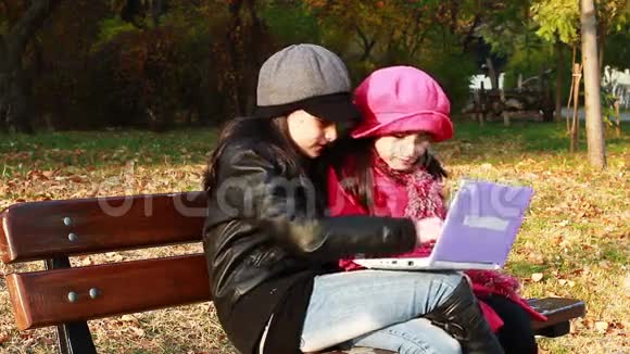 两个小女孩坐在长凳上玩笔记本电脑视频的预览图