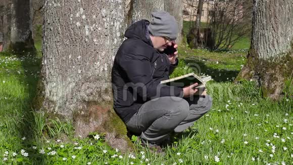 在树附近的草地上人们在看书和打智能电话视频的预览图