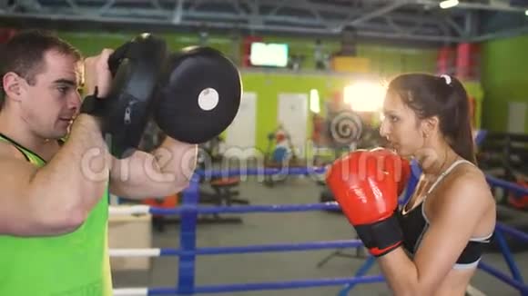 年轻女子拳击手与她的教练在拳击场训练赛前热身视频的预览图