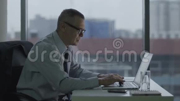 老商人在现代办公室里用电脑工作他的背疼视频的预览图