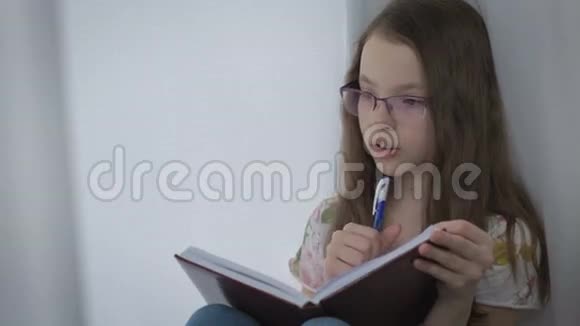 戴眼镜的漂亮小女孩勤奋地在窗口做作业视频的预览图