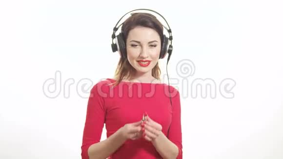 可爱的红色女孩听着大耳机里的音乐跳舞玩得很开心把红色口红涂在白色上视频的预览图
