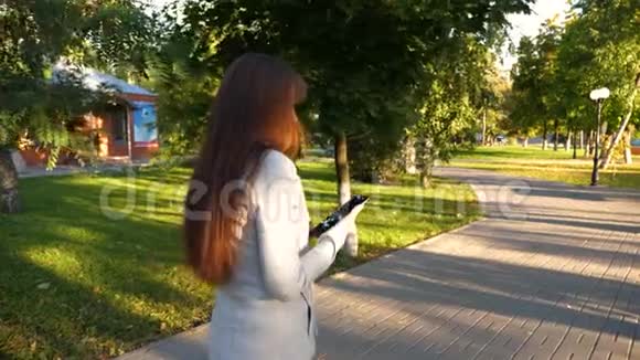 穿着轻便商务套装带平板电脑的女孩上班了美丽的女商人走在公园的小巷里里面有平板电脑视频的预览图