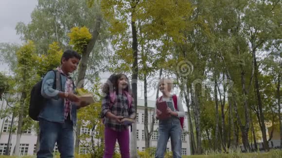 回学校去三个朋友背包拥抱和笑在学校前面学校儿童混合种族团体视频的预览图