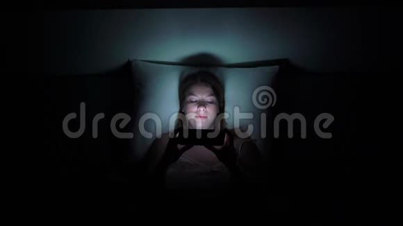 年轻女子在晚上睡觉前在床上使用手机手机成瘾的概念视频的预览图