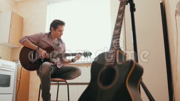 年轻人用吉他作曲在厨房里演奏其他乐器在前台视频的预览图