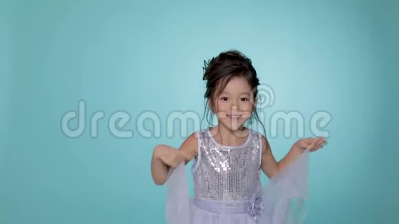 漂亮的小女孩穿着银色的裙子在蓝色的背景上跳舞视频的预览图