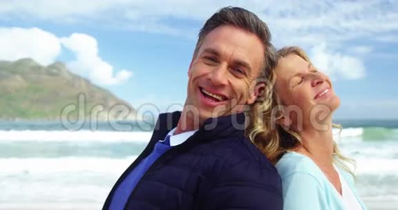 成熟的夫妻背靠背站在海滩上视频的预览图