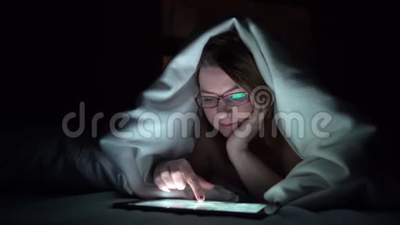 年轻女子在晚上睡觉前在床上用平板电脑手机成瘾的概念视频的预览图