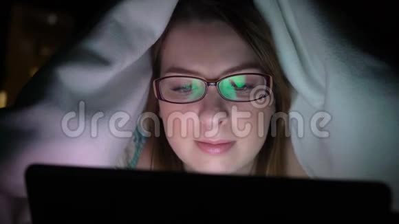 年轻女子在晚上睡觉前在床上用平板电脑手机成瘾的概念视频的预览图