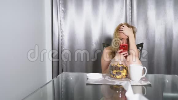 饥肠辘辘的伤心女人晚上坐在客厅的桌子旁吃着肝脏用着智能手机视频的预览图
