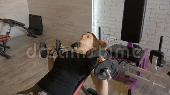 年轻漂亮的女孩在健身房用哑铃做运动视频的预览图
