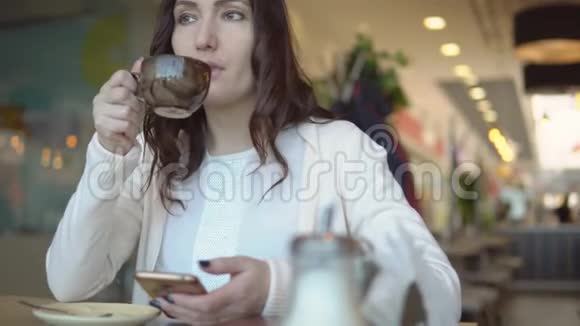 一位美丽的黑发女人在咖啡馆的餐桌上打电话视频的预览图