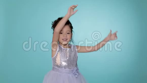 漂亮的小女孩穿着银色的裙子在蓝色的背景上跳舞视频的预览图