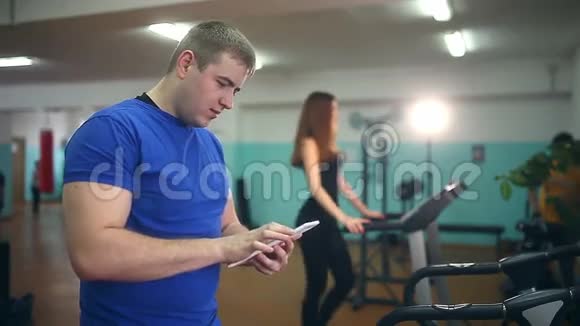 男教练在健身房女孩与平板电脑跑步机健身健康的生活方式运动视频的预览图