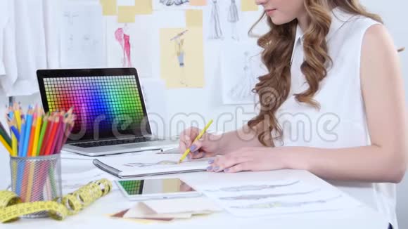 时装设计师为新的收藏品绘制草图然后看电脑视频的预览图