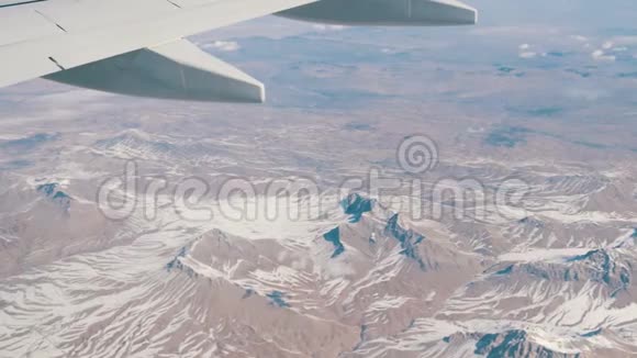 令人惊叹的山脉美景微微覆盖着雪从云中掠过从飞机窗口眺望视频的预览图