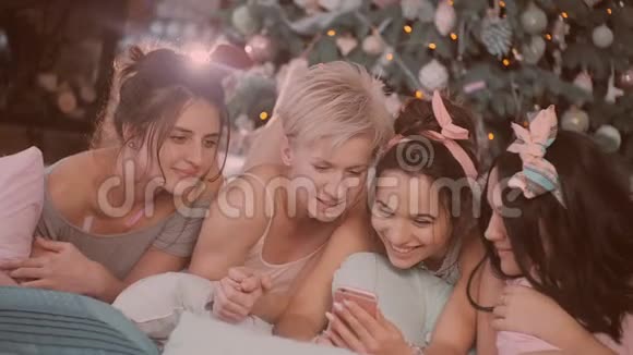 帕贾马派对穿睡衣的女孩在圣诞树附近玩视频的预览图
