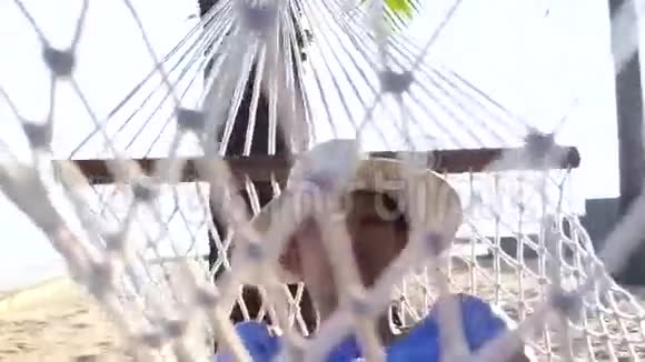 视频亚洲女人戴帽子的女孩在阳光明媚的海滩上用椰子树在吊床上放松视频的预览图
