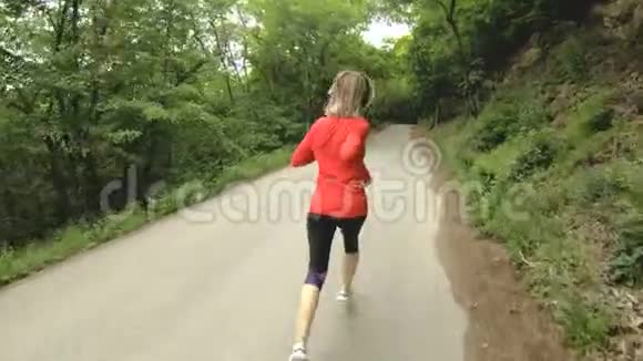 奔跑的女孩在夏季森林里做户外运动的金发女孩后视慢动作广角视频的预览图