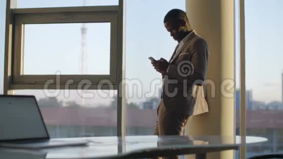 穿着西装的年轻黑人商人在阳光下靠窗站在办公室里视频的预览图