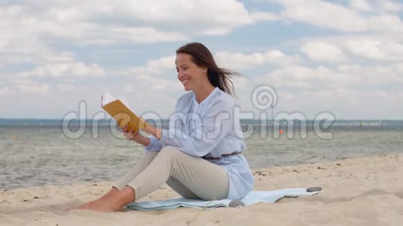 快乐微笑的女人在夏日海滩上看书视频的预览图
