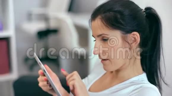 漂亮的女人坐在沙发上用平板电脑视频的预览图