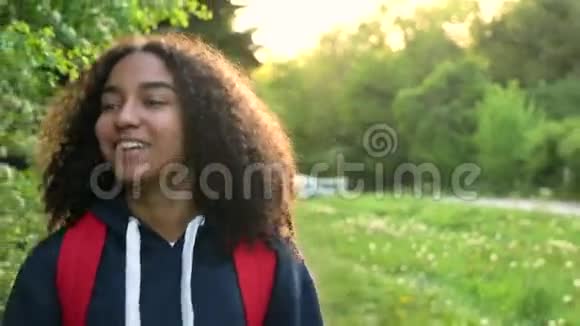 美丽的快乐混血非裔美国少女少女年轻女性日落时带着红色背包在乡下徒步旅行视频的预览图
