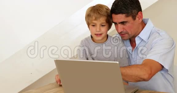 小男孩和他的父亲在桌旁用笔记本电脑视频的预览图