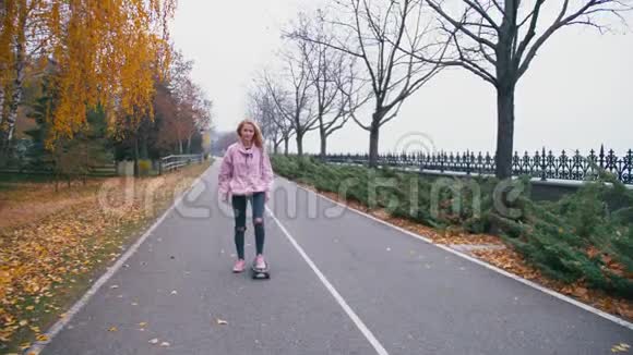 年轻漂亮的金发女郎穿着粉红色的风挡玩滑板滑着长板下山视频的预览图