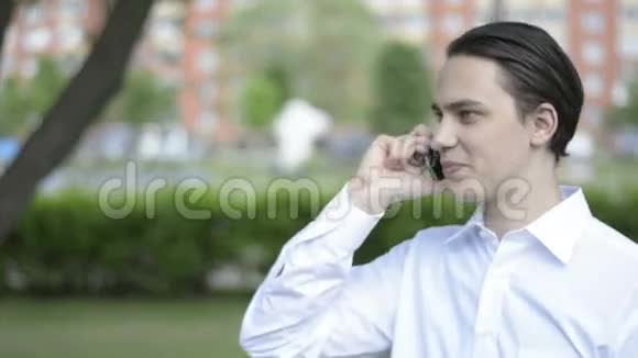 在公园里用手机说话的年轻人视频的预览图