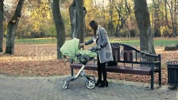 年轻的母亲在秋天的公园里和一辆马车一起散步视频的预览图