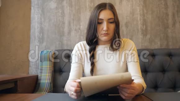一个年轻的女人坐在有菜单的咖啡馆里视频的预览图
