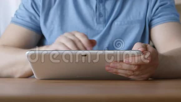 一只手拿着平板电脑的年轻人在家里的桌子上视频的预览图