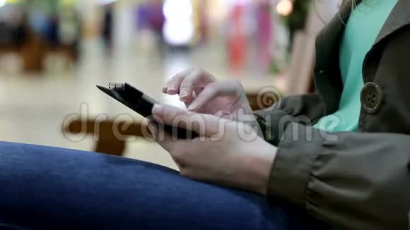 有平板电脑的年轻女子坐在商场的长椅上视频的预览图